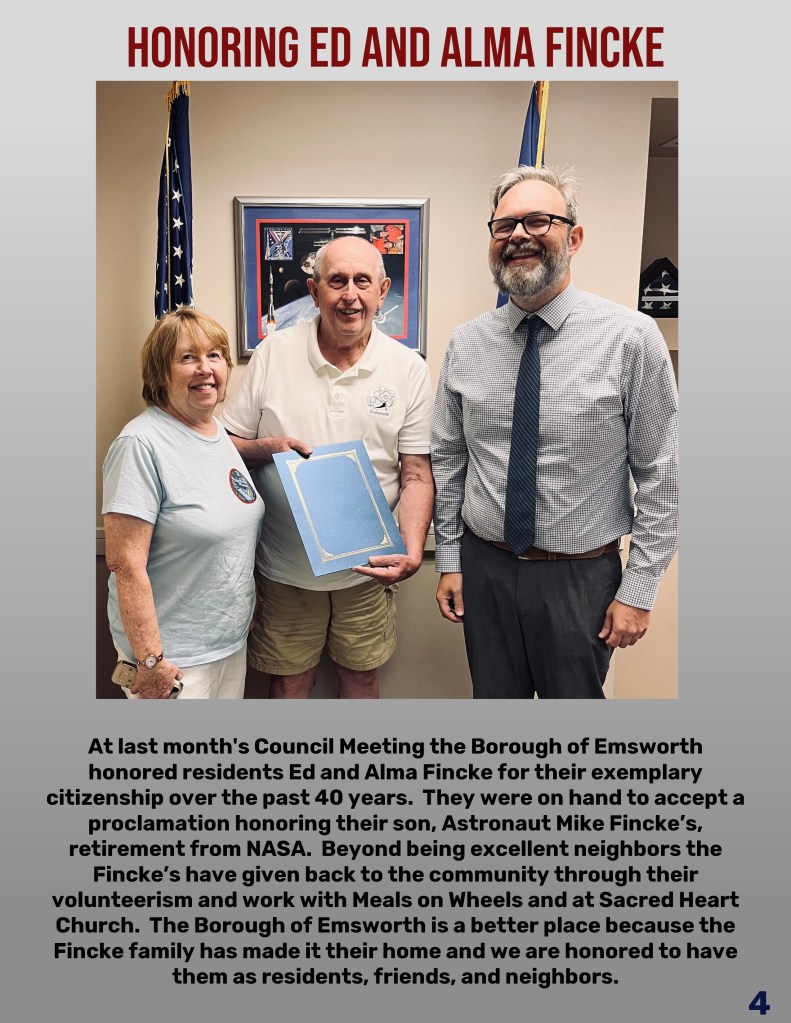 Three individuals standing together in an office setting, honoring Ed and Alma Fincke for their contributions to the community. The man in the center holds a proclamation, with a framed picture of a space mission in the background.